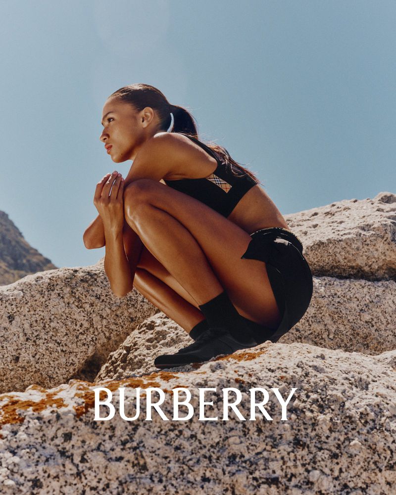 Model crouching on granite rocks against a clear blue sky wearing black athletic wear for Burberry.