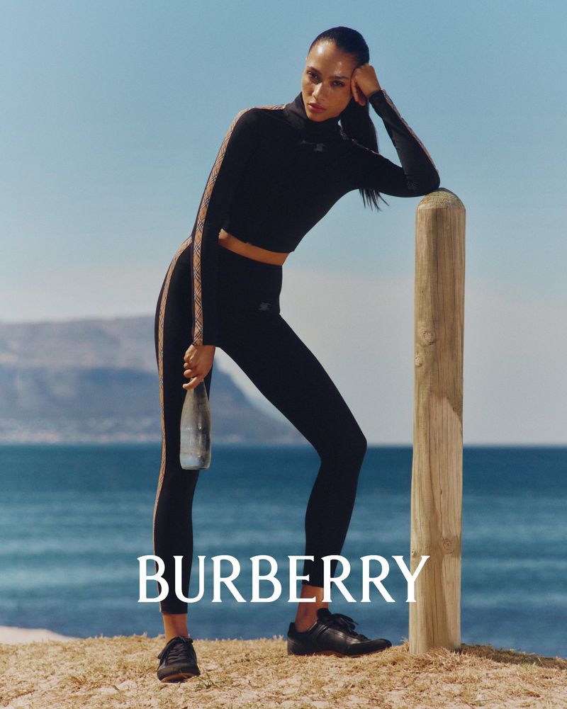 Model leaning against a wooden post on a coastal shore wearing black athletic wear by Burberry