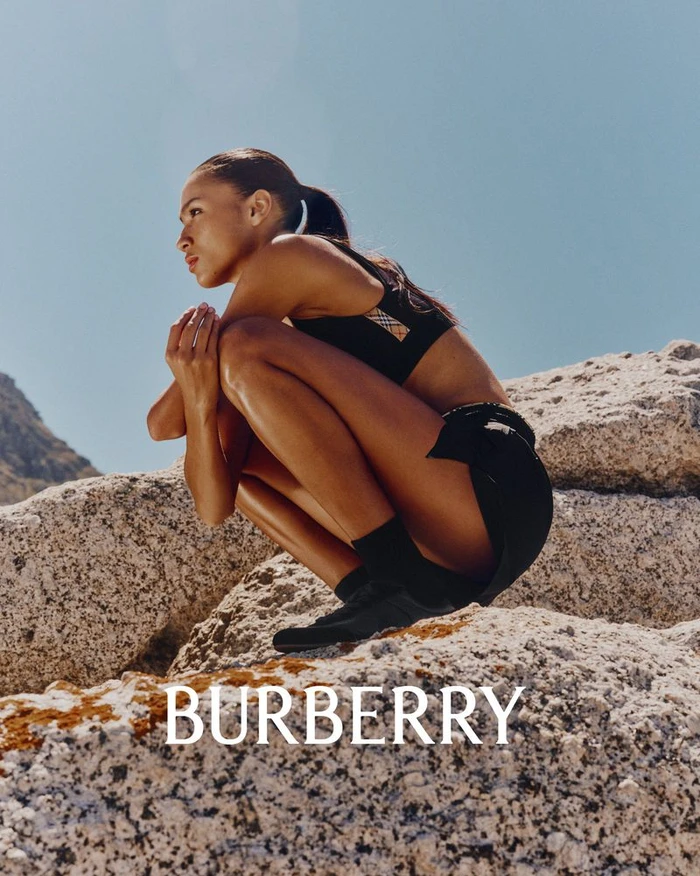 Model crouching on granite rocks against a clear blue sky wearing black athletic wear for Burberry.