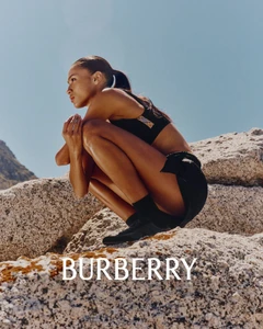 Model crouching on granite rocks against a clear blue sky wearing black athletic wear for Burberry.