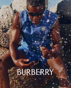 Model wearing blue athletic vest and sunglasses sitting among rocky boulders with splashing water drops