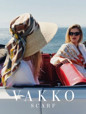 Two women in a convertible car near the ocean, wearing printed silk scarves and sunglasses under bright sunlight
