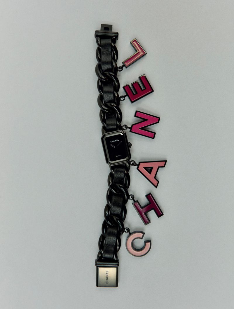 Chanel Première watch with black chain-link bracelet and letter charms, studio shot against a light gray background.