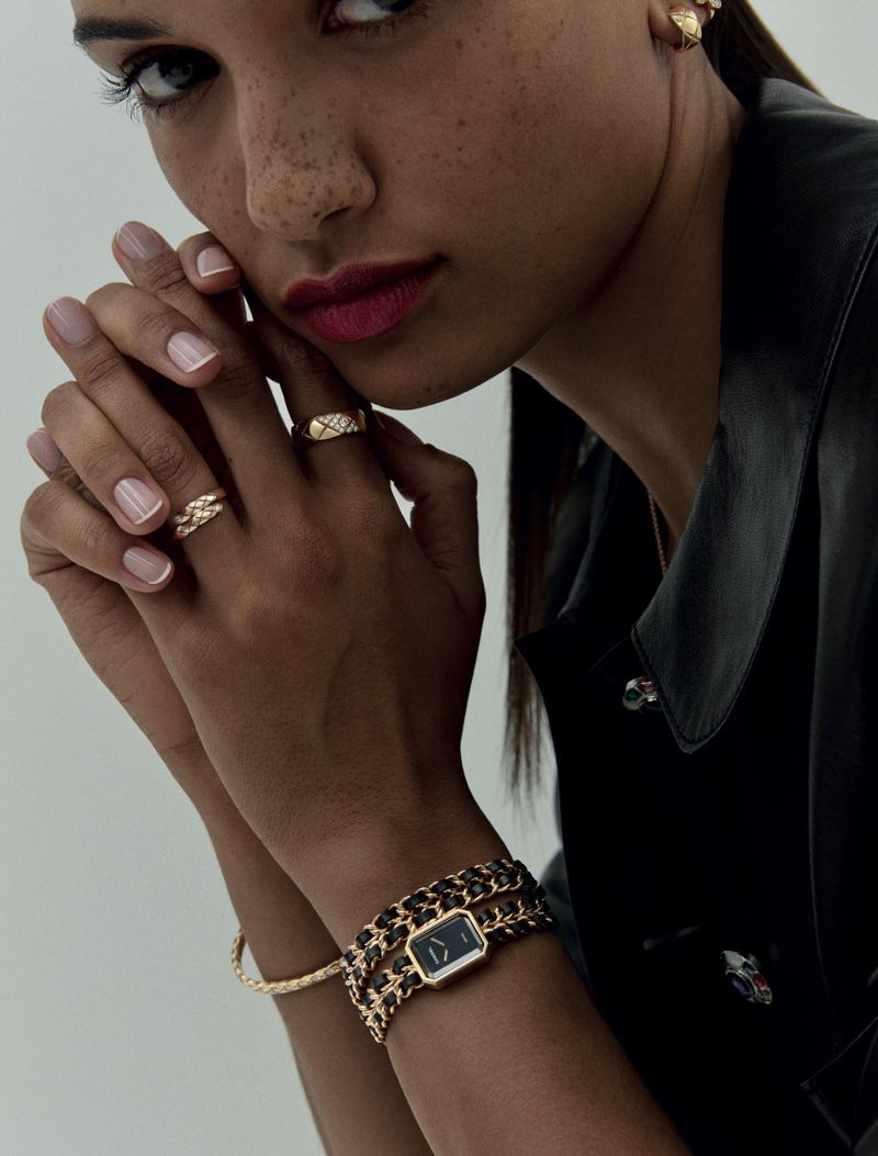 Close-up of a woman showcasing luxury jewelry, including rings and a watch, with a blurred background and soft, diffused lighting.