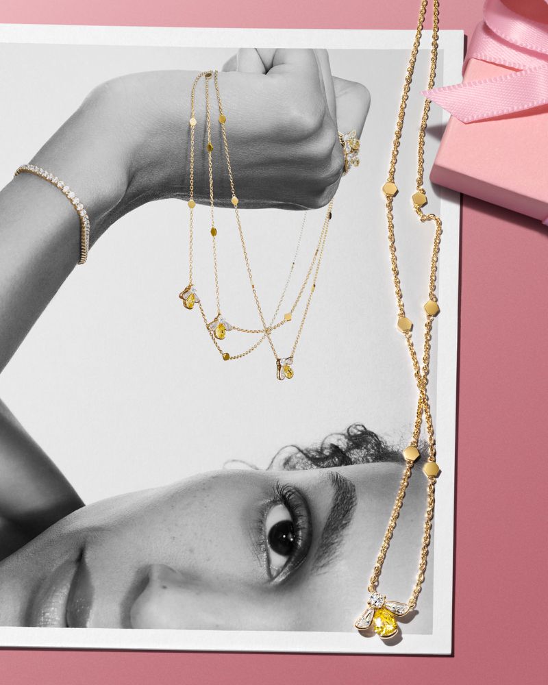 Gold necklaces and bracelet displayed over a black and white print featuring a model's face against a pink background