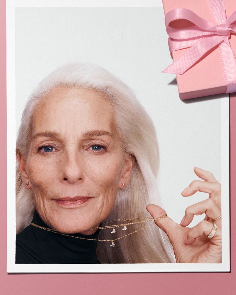 Elderly woman with long white hair wearing a dark top and delicate gold necklaces for Pandora