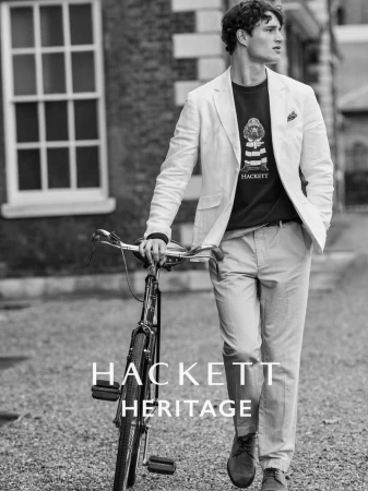 Black and white portrait of a man in a blazer with a bicycle on a cobblestone street, featuring a building with a window in the background.