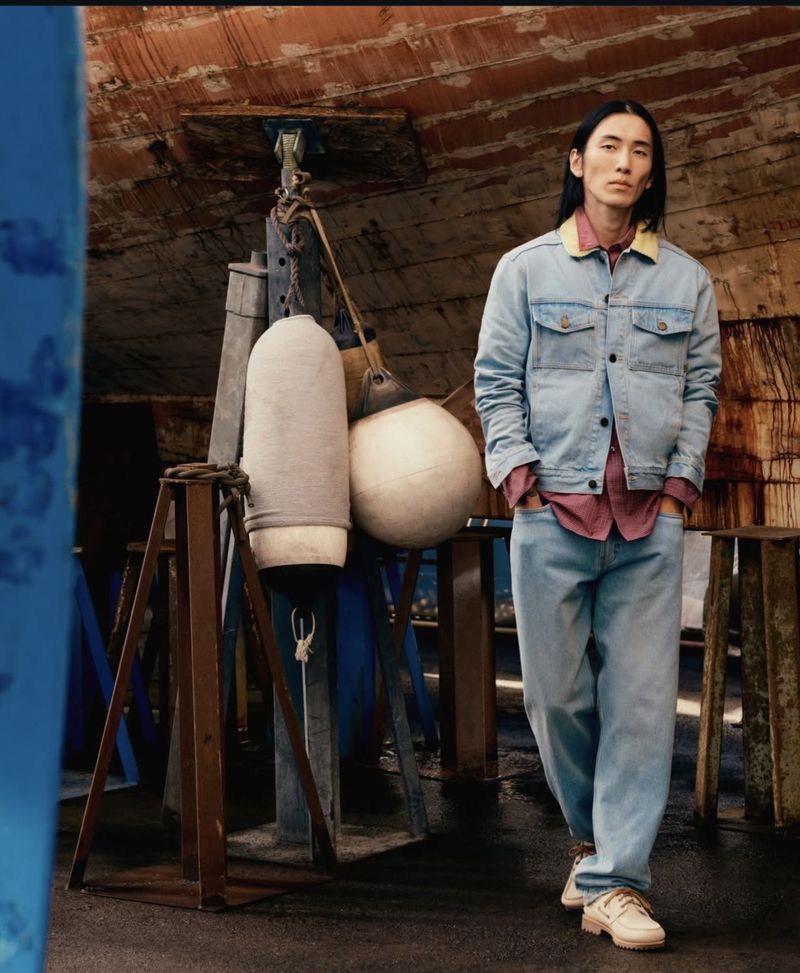 Model Hyuk Kim wearing denim jacket and boat shoes standing in boatyard near buoys