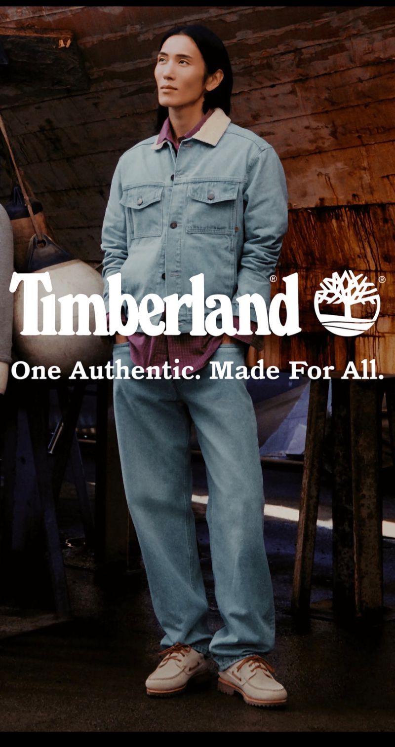 Model wearing a light blue denim jacket and matching jeans standing against a weathered wooden background with boat shoes