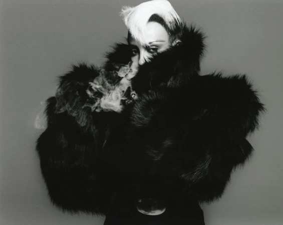 Striking black and white studio portrait of an adult female wearing a voluminous fur coat and elaborate platinum hairstyle.