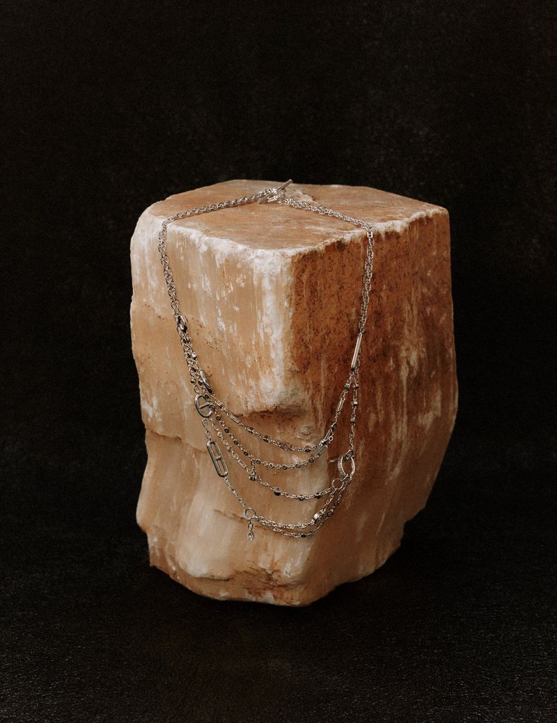 Delicate silver layered necklace draped over a rough textured orange and white stone block against a dark background