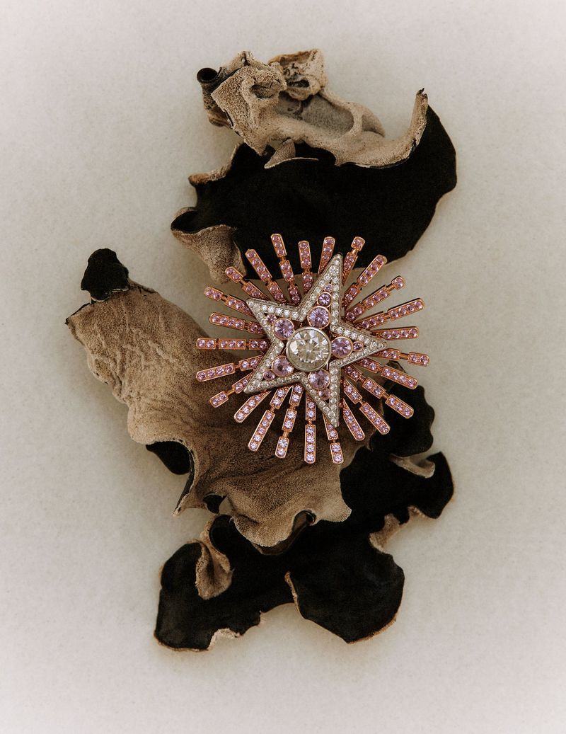 Elegant star-shaped brooch featuring pink and purple gems with a central diamond, displayed on textured material against a light background.