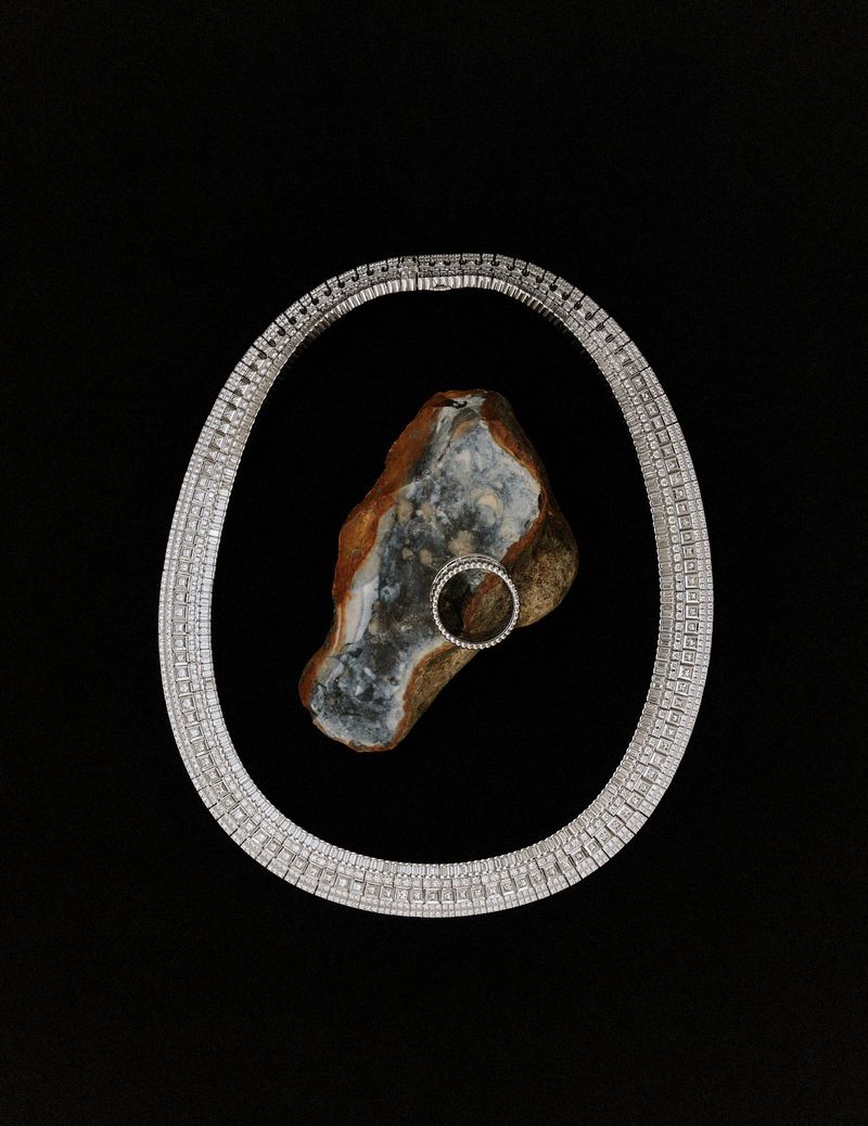 Diamond necklace and ring arranged around a textured stone on a solid black background for Manifesto Magazine