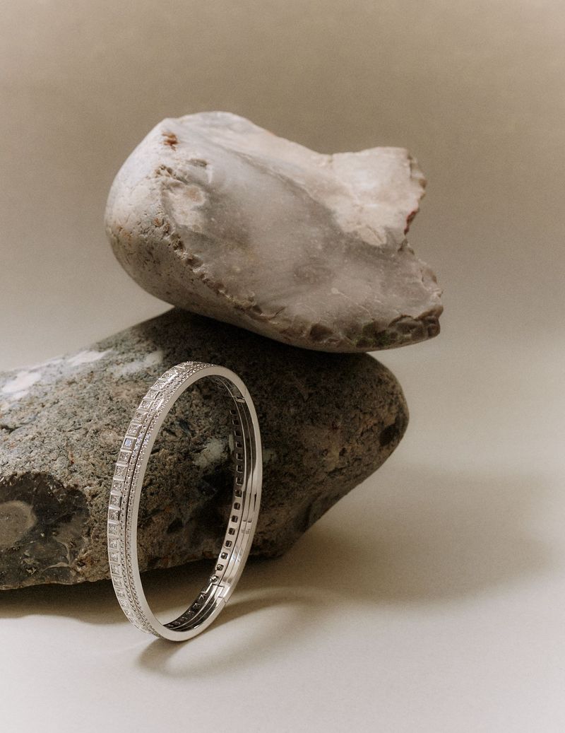 Silver diamond bracelet resting against smooth grey stones on a neutral backdrop