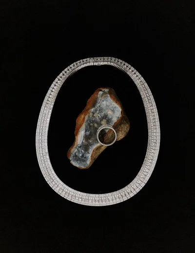 Diamond necklace and ring arranged around a textured stone on a solid black background for Manifesto Magazine