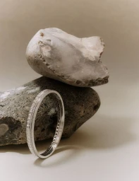 Silver diamond bracelet resting against smooth grey stones on a neutral backdrop