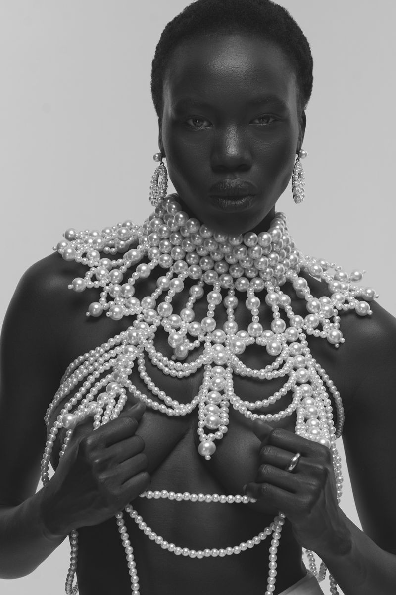Black woman wearing elaborate pearl necklace and earrings against a plain background for Glamour Magazine U.S.