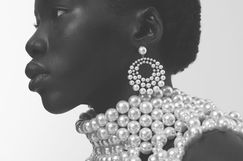 Close-up profile of a black woman wearing large pearl hoop earrings and a heavy pearl collar necklace.