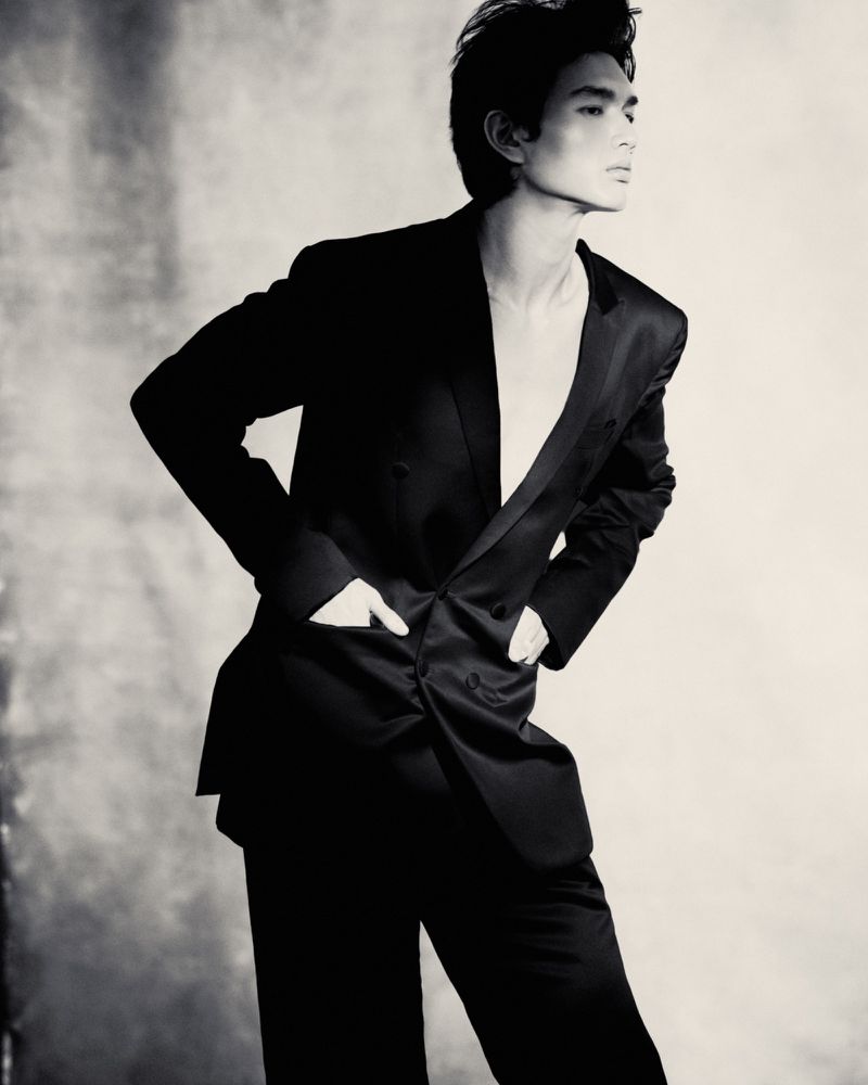 Monochrome portrait of a male model wearing a black suit jacket and trousers against a textured background.