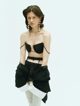 Model wearing a black top and white tights against a plain light background