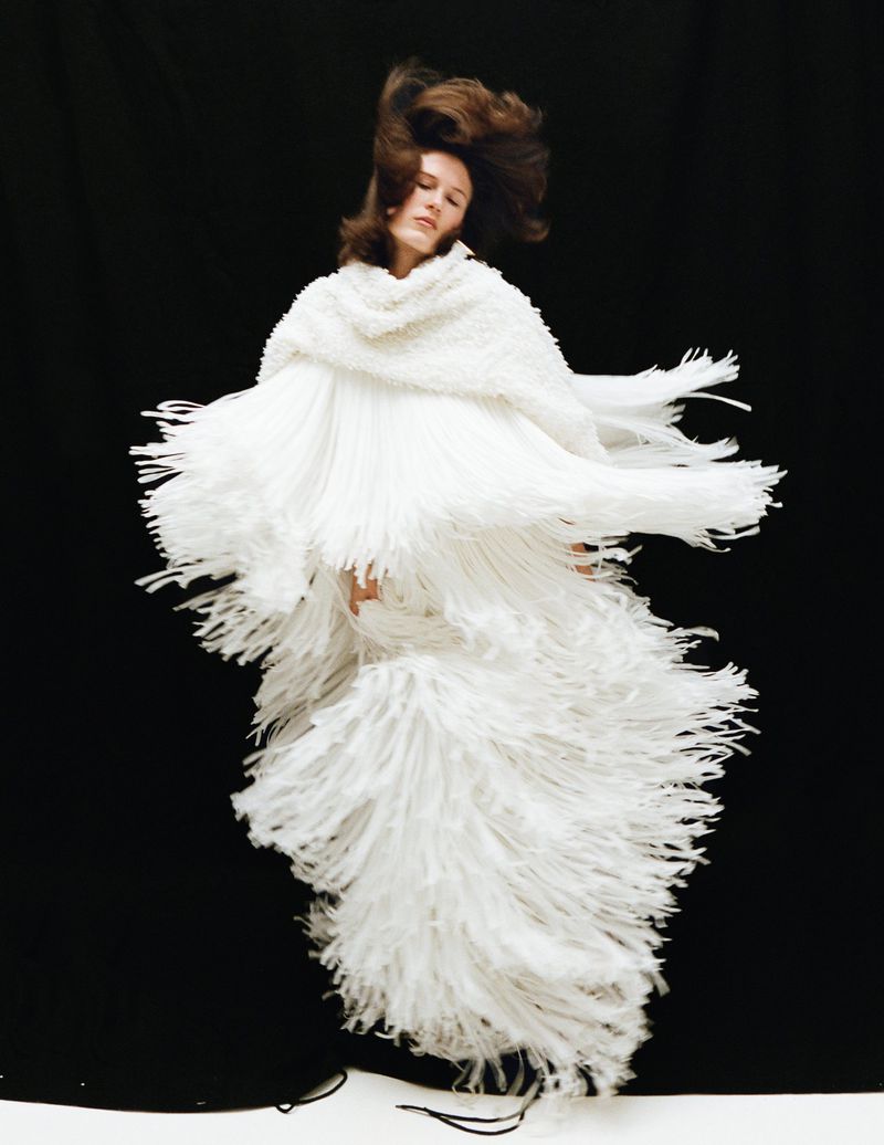 Model wearing a textured white fringed gown with dynamic motion against a black background