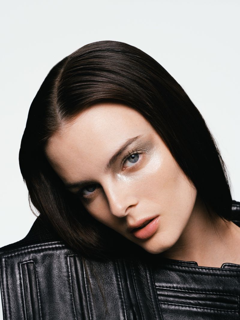 Close-up beauty shot of a dark-haired woman wearing glitter eye makeup and a black leather jacket, set against a white backdrop.