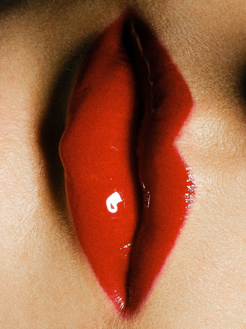 Close-up of human lips with glossy red lipstick. Focus on texture and form, highlighting the makeup and skin details.