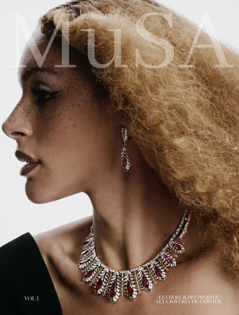 Close-up of a woman with blonde curly hair wearing an ornate ruby and diamond necklace and earrings, with a white background and overlayed text.