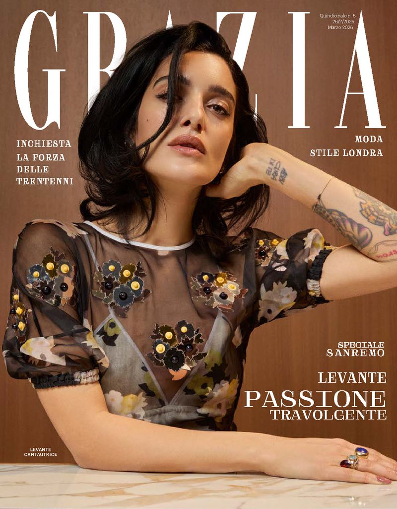 Grazia magazine cover featuring a woman with dark hair wearing a sheer, floral-embellished top, accessorized with rings, posing indoors.
