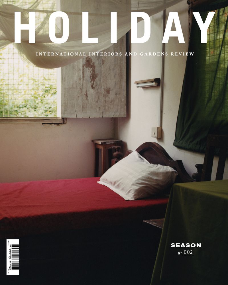 Interior of a bedroom with a red bed, white pillow, and view to the outside. 'Holiday' magazine cover featured.