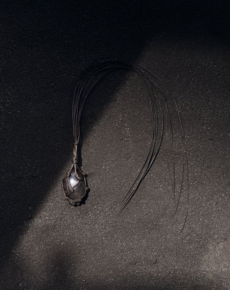 Close-up of a dark-toned pendant necklace with a wire wrap design on a textured black surface in a moody, artistic composition.