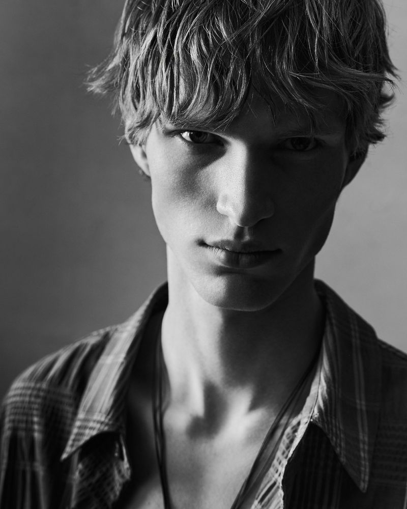 Close up portrait of a young male model with tousled hair wearing a collared shirt against a neutral studio background