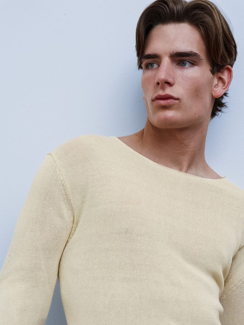 Young man wearing a light yellow knitted sweater against a pale blue background