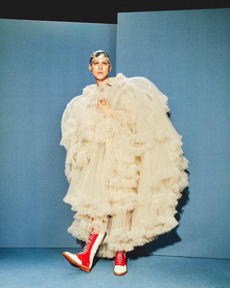 Tommy Dorfman in voluminous white tulle gown and red boots against blue backdrop for Financial Times HTSI Magazine