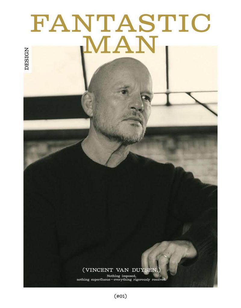 Portrait of bald man in black crewneck sweater looking slightly away against a dark architectural interior background