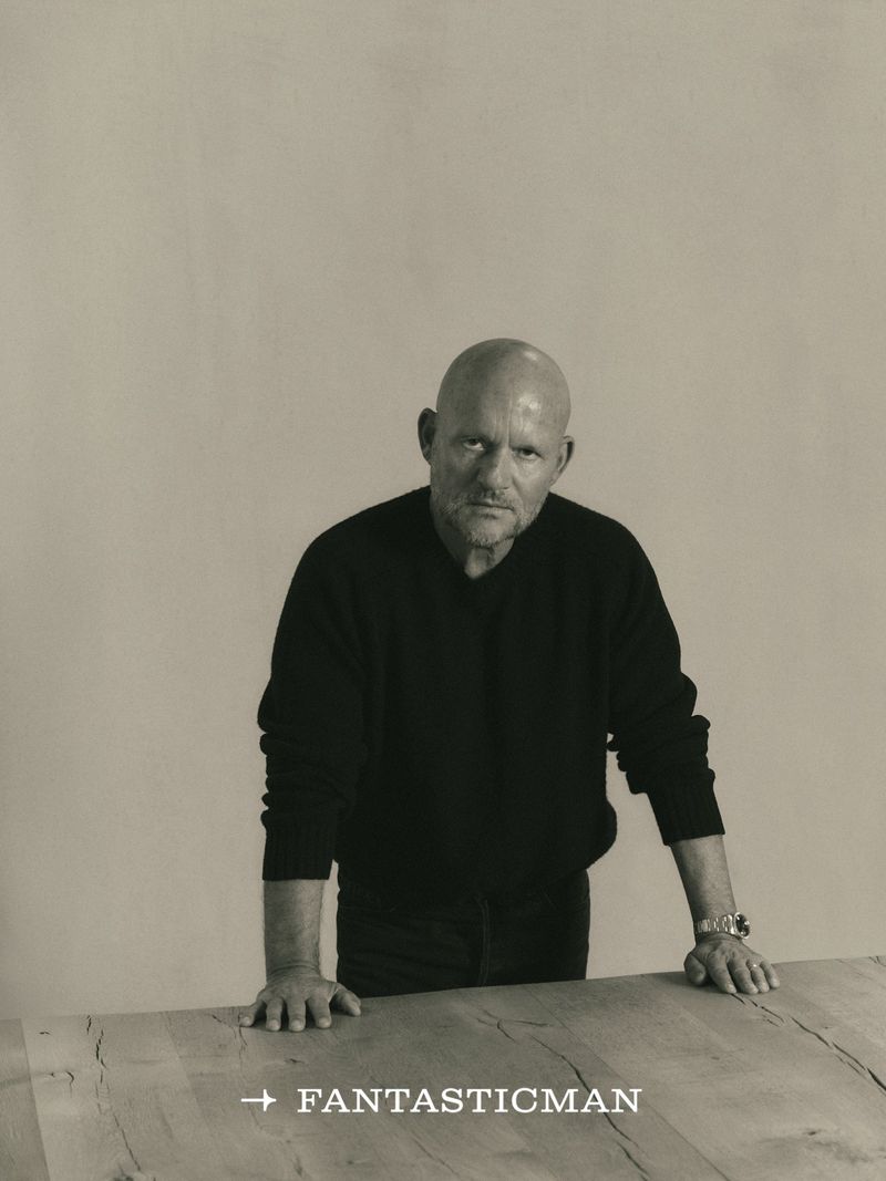 Portrait of a bald man leaning on a wooden table against a plain neutral background for Fantastic Man China