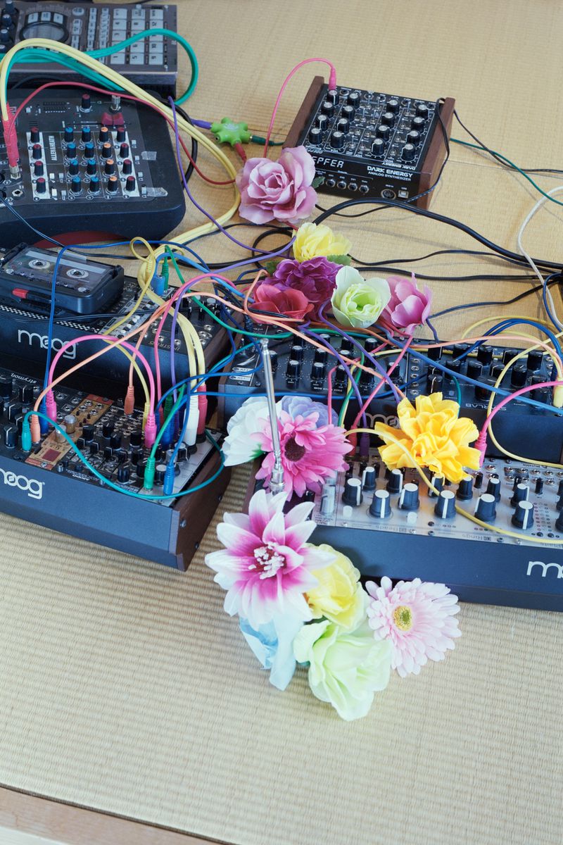 Modular synthesizers connected with colorful patch cables intertwined with artificial flowers on a tatami mat