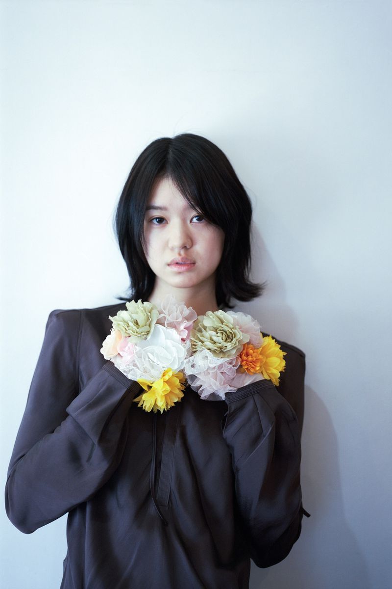 Portrait of a young woman wearing a dark brown top holding delicate clusters of colorful fabric flowers.