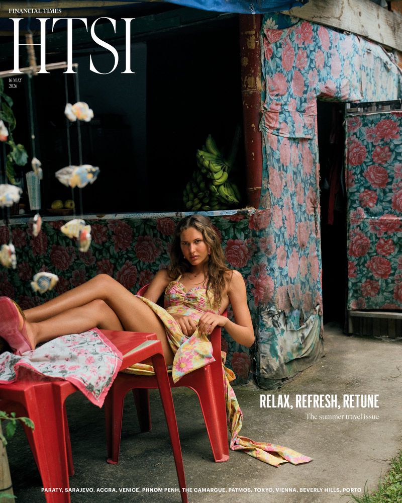 Magazine cover featuring a woman in a floral outfit relaxing on a red plastic chair outside a floral wallpapered structure.