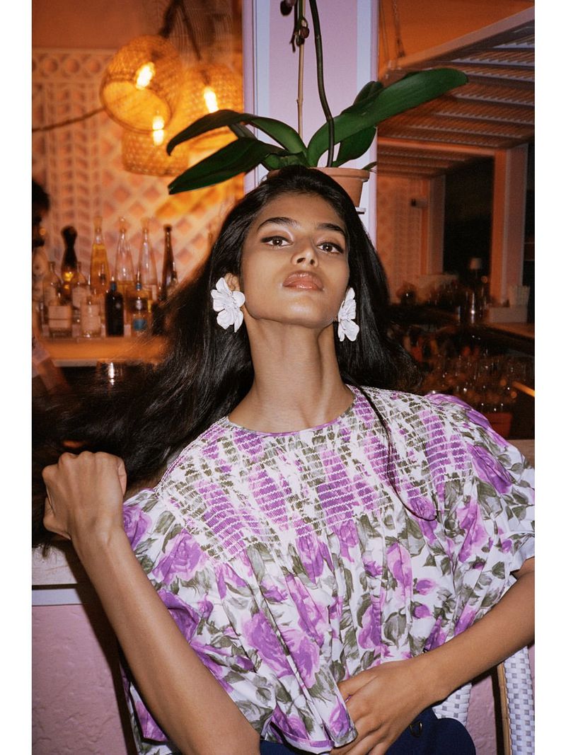 Model Bhavitha Mandava wearing white flower earrings and a purple floral patterned blouse in a hospitality venue