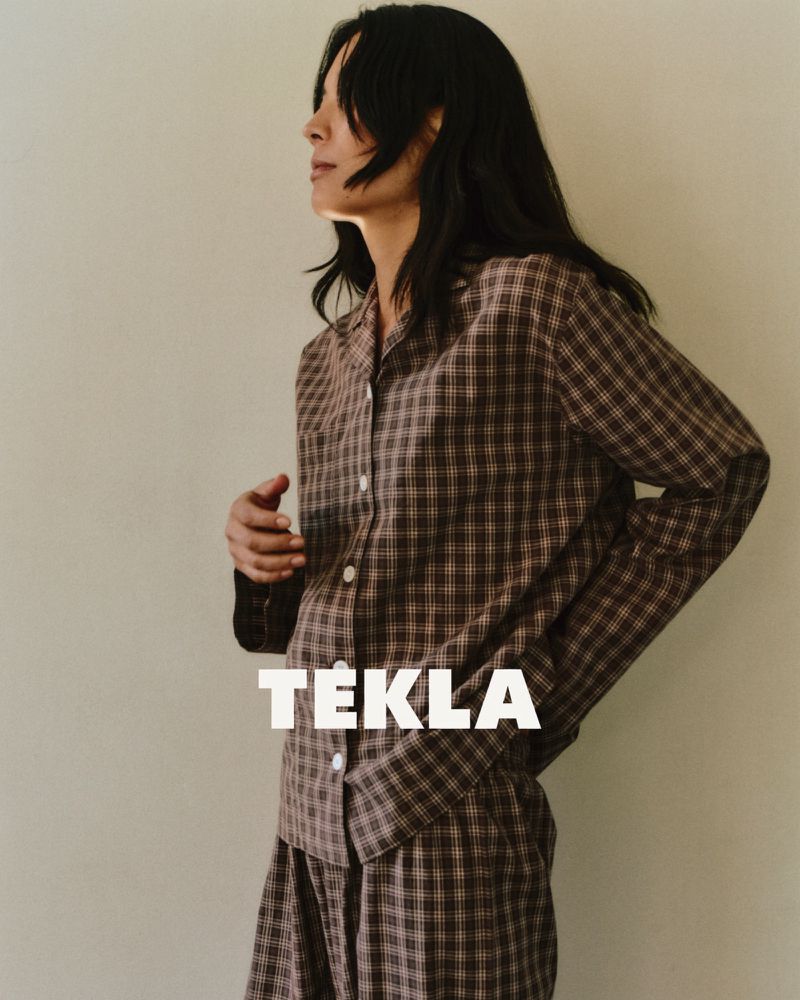Model wearing a brown plaid pajama set against a neutral wall for Tekla sleepwear campaign.
