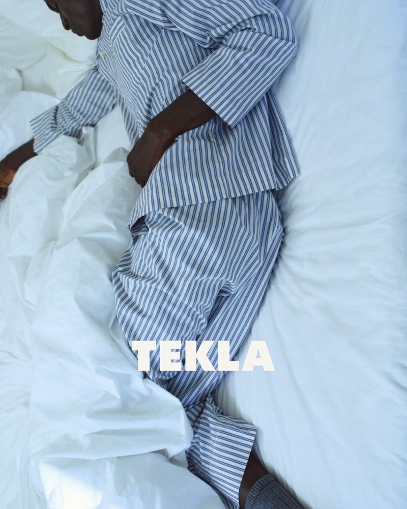 Model lying in white bedsheets wearing blue and white striped pyjamas for Tekla