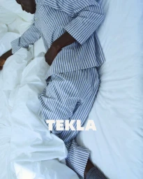 Model lying in white bedsheets wearing blue and white striped pyjamas for Tekla