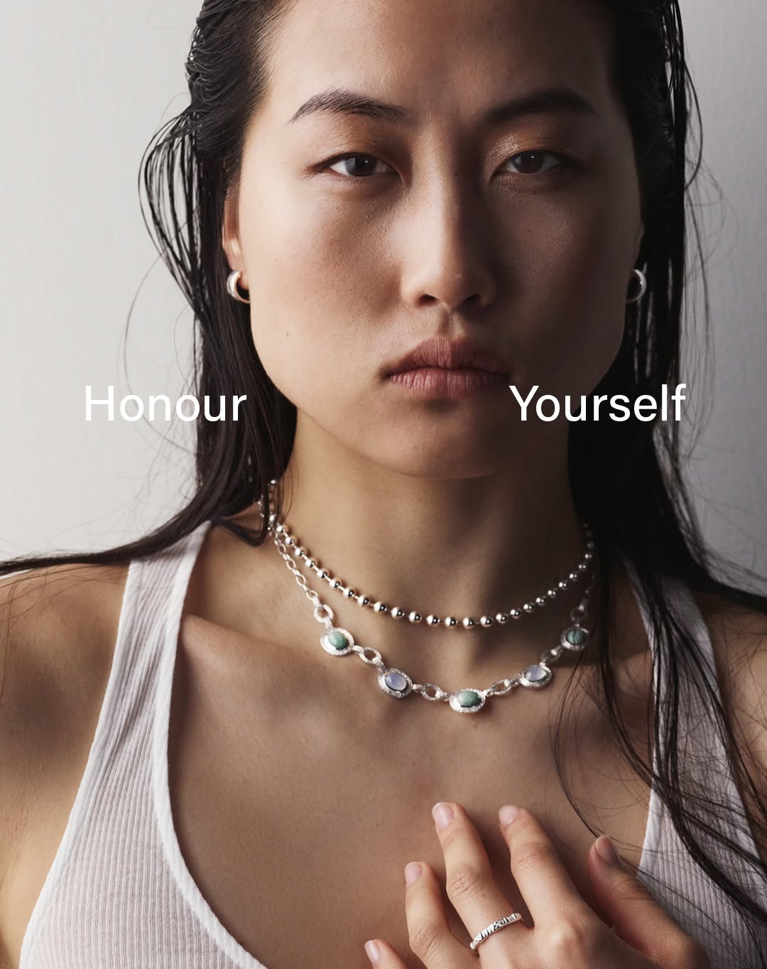 Close-up studio shot of an Asian female model with silver necklaces and a white tank top, featuring the text 'Honour Yourself'.