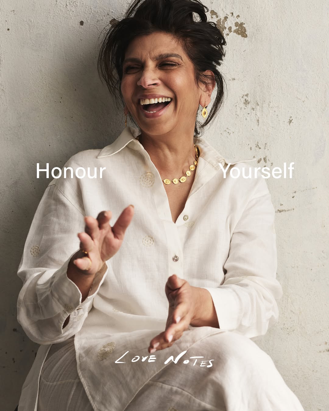 Laughing woman in white shirt and pants, wearing gold necklace and earrings, with love notes text overlay, smiles outdoors.