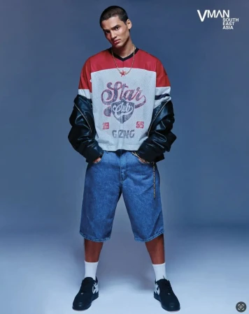 Full-body portrait of a young adult male fashion model in a vintage-style outfit, including jean shorts, sneakers and a mesh top.