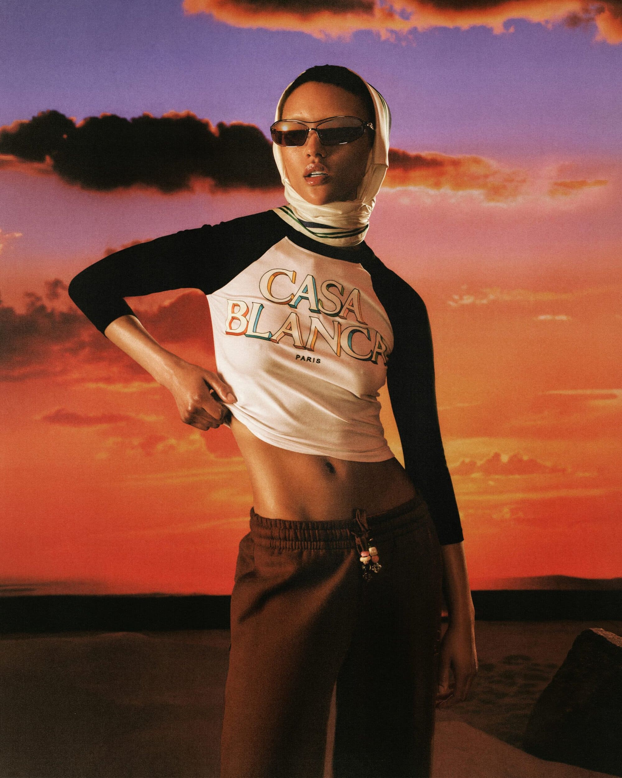 Model wearing Casablanca branded raglan t-shirt and sunglasses against sunset sky background