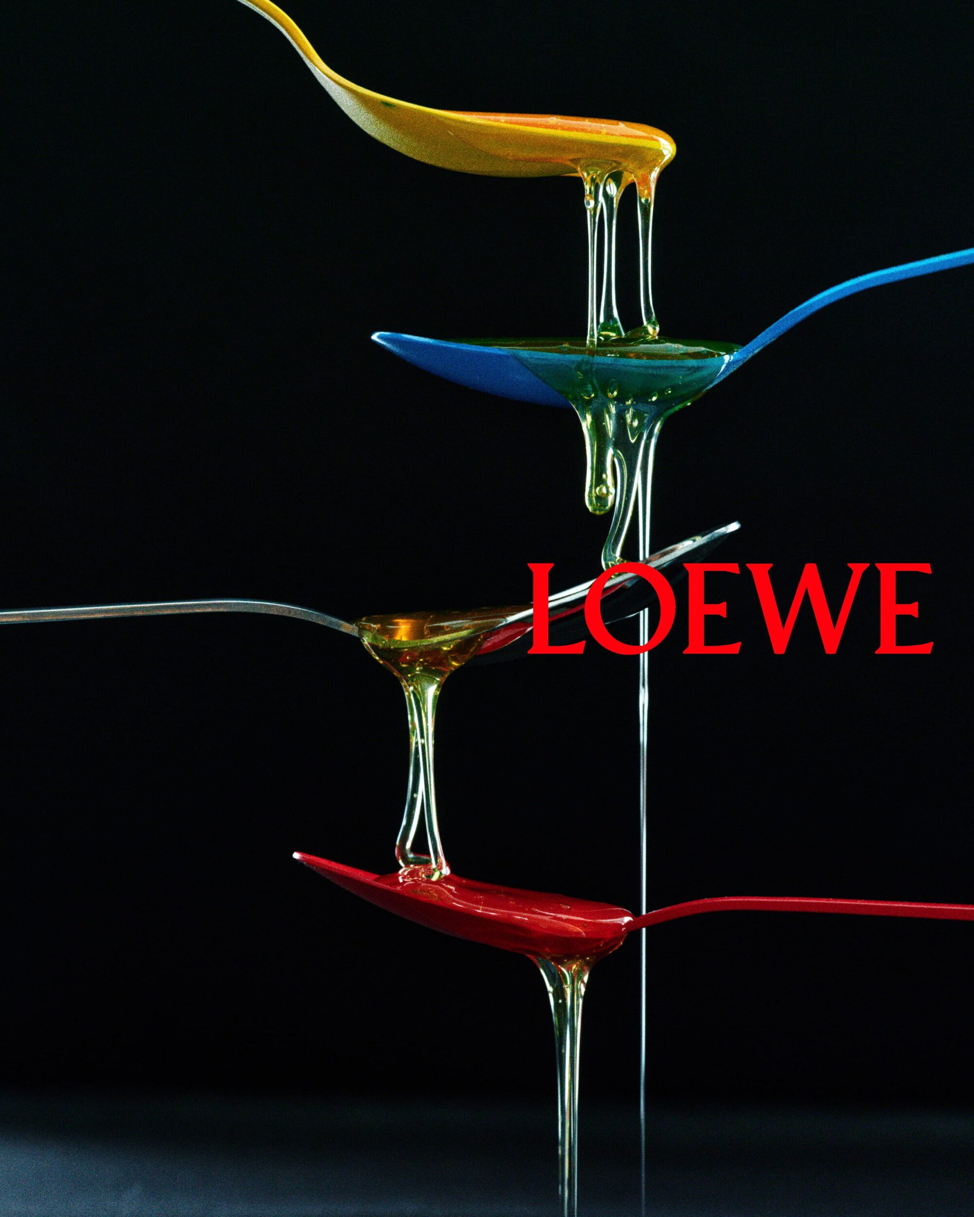 Four colorful stacked spoons dripping viscous amber liquid against a black background