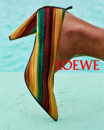 Close-up of a high-heeled shoe featuring multicolored vertical stripes of green, yellow, and brown against a turquoise pool background.