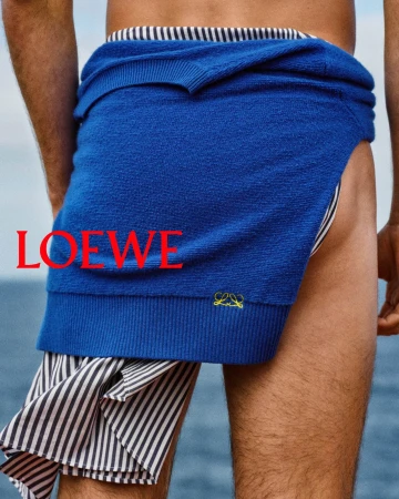 Close-up rear view of a person wearing a royal blue sweater tied around the waist over striped shorts against an ocean background.